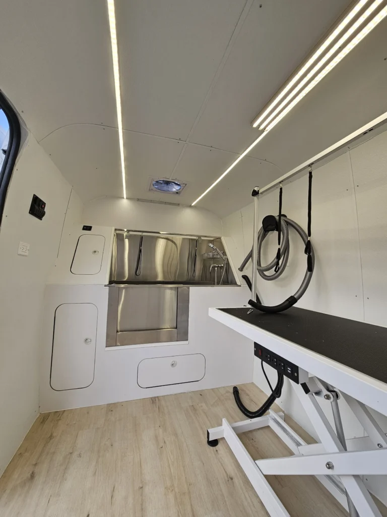 Interior of a mobile pet grooming van with a grooming table and washing station.
