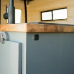 Close-up of a kitchen countertop with a switch on a gray cabinet, in a wooden kitchen with windows in the background.