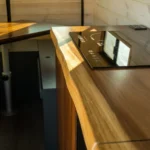 Close-up of a wooden kitchen counter with a black glass induction cooktop, reflecting a window, in a modern kitchen with wooden walls.