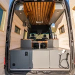 Interior of a converted van with wooden walls and ceiling, gray cabinetry, and two black front seats.