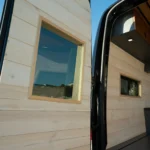 Interior of a tiny home or van with wooden walls and ceiling, featuring small windows and modern lighting.
