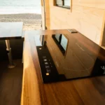 Interior of a small kitchen with a wooden countertop, an induction cooktop, a window, and a small foldable table.